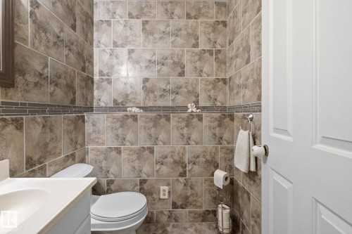 Bathroom featuring floor-to-ceiling large format wall tiling, a decorative glass mosaic accent border, and a white two-panel door - 18126 98 Avenue, Edmonton, AB 