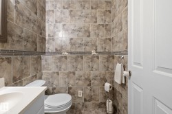 Bathroom featuring floor-to-ceiling large format wall tiling, a decorative glass mosaic accent border, and a white two-panel door - 