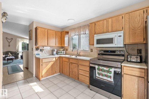 Kitchen featuring wood cabinetry, white tile flooring, a stainless steel range, and a built-in microwave - 18126 98 Avenue, Edmonton, AB 