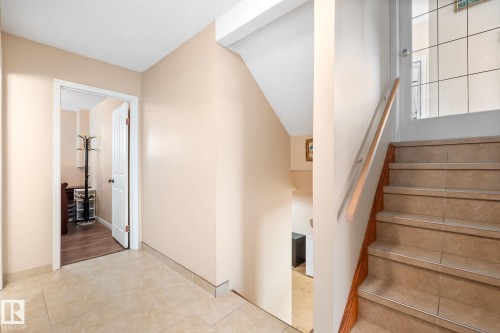 Foyer featuring neutral wall paint, tile flooring, and a staircase with a wood-finish handrail and tile treads - 18126 98 Avenue, Edmonton, AB 
