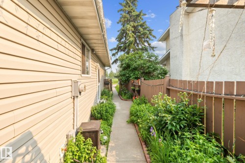 Sidewalk pathway featuring established garden beds, a privacy fence, and a neutral-toned vinyl-sided exterior - 18126 98 Avenue, Edmonton, AB 