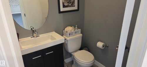 Compact bathroom featuring a white toilet, contemporary vanity with a chrome faucet, and a round wall mirror - 16505 133 Street, Edmonton, AB 