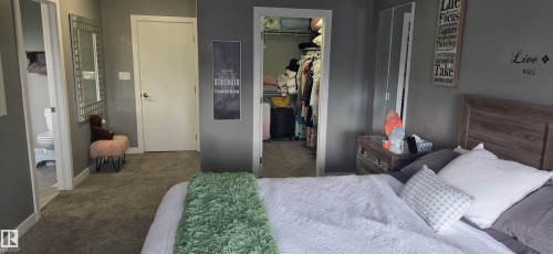 Carpeted bedroom featuring a walk-in closet, a wood-finish headboard, and a neutral color palette - 16505 133 Street, Edmonton, AB 