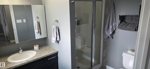 Bathroom featuring a granite-look countertop, undermount sink, dark wood-finish vanity, and a glass-enclosed shower - 16505 133 Street, Edmonton, AB 