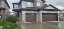 Contemporary duplex featuring light-toned siding, stone veneer accents, dark shingle roofing, dark brown garage doors with upper window panels, and a concrete driveway - 16505 133 Street, Edmonton, AB 