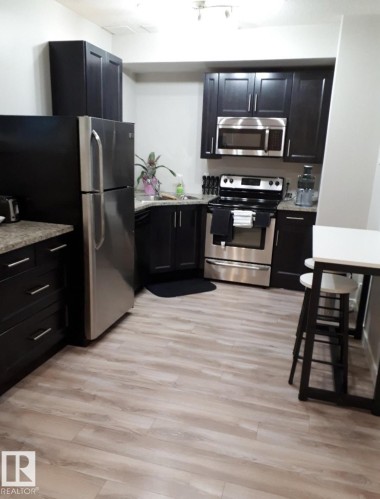 Kitchen featuring dark cabinetry, stainless steel appliances, speckled countertops, and wood-finish flooring - 16505 133 Street, Edmonton, AB 