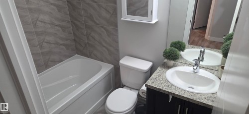 Full bathroom featuring a white tub, toilet, and vanity with an integrated sink - 16505 133 Street, Edmonton, AB 