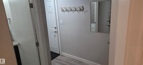 Entryway featuring wood-finish flooring, a white paneled door, and a wall-mounted coat rack - 16505 133 Street, Edmonton, AB 