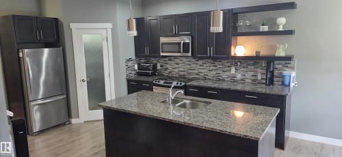 Contemporary kitchen featuring dark cabinetry, stainless steel appliances, and a mosaic tile backsplash - 16505 133 Street, Edmonton, AB 