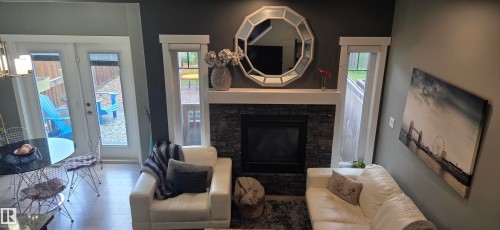 Living area featuring a floor-to-ceiling stone fireplace with a white mantel, complemented by a large octagonal mirror - 16505 133 Street, Edmonton, AB 