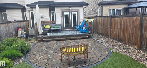 Patio area featuring irregular flagstone pavers, a wood deck with double doors, privacy fencing, a landscaped border with shrubs, and an artificial turf section - 16505 133 Street, Edmonton, AB 