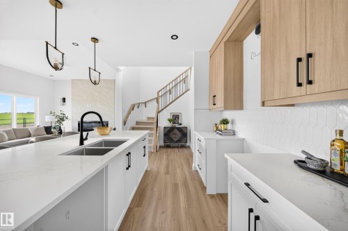 Spacious kitchen featuring a large island with an undermount double sink and matte black faucet, white shaker-style cabinetry, light wood-finish upper cabinetry, and white pickett tile backsplash - 523 Ashgrove Circle, Leduc, AB 