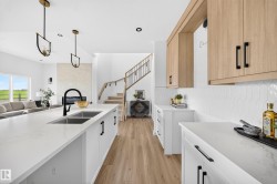 Spacious kitchen featuring a large island with an undermount double sink and matte black faucet, white shaker-style cabinetry, light wood-finish upper cabinetry, and white pickett tile backsplash - 
