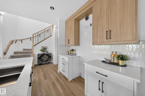 Contemporary kitchen with light wood-finish upper cabinetry, white lower cabinetry, and black hardware - 523 Ashgrove Circle, Leduc, AB 
