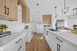 Bright kitchen featuring wood-finish flooring, white perimeter cabinetry, and an expansive center island with a double basin sink and matte black faucet - 