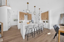 Kitchen featuring a large central island with seating, white shaker-style base cabinetry, wood-finish upper cabinetry, and a white subway tile backsplash - 