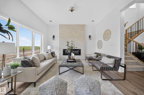 Bright living area featuring a floor-to-ceiling fireplace with stone surround, ample natural light from large windows, wood-finish flooring, and a multi-level staircase with wood railings and black spindles - 523 Ashgrove Circle, Leduc, AB 