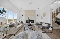 Bright living area featuring a floor-to-ceiling fireplace with stone surround, ample natural light from large windows, wood-finish flooring, and a multi-level staircase with wood railings and black spindles - 