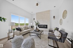 Spacious living area featuring large windows, a built-in linear fireplace with a light-toned stone surround, recessed lighting, and wood-finish flooring - 