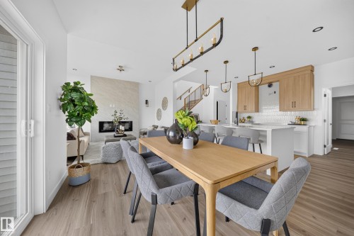 Open-concept living area featuring wood-finish flooring, a contemporary linear fireplace with a stone surround, and a kitchen with light wood cabinetry and a white tiled backsplash - 523 Ashgrove Circle, Leduc, AB 