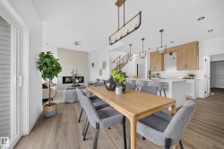 Open-concept living area featuring wood-finish flooring, a contemporary linear fireplace with a stone surround, and a kitchen with light wood cabinetry and a white tiled backsplash - 