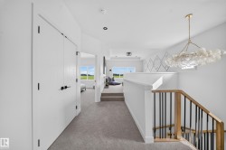 Upper-level hallway featuring a contemporary chandelier, white walls, and gray carpeting - 