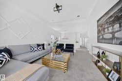 Spacious living area featuring light gray carpeting, a decorative accent wall with geometric molding, and recessed lighting - 