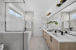 Modern bathroom featuring a dual vanity with light wood-finish cabinetry, white countertops, and black fixtures - 