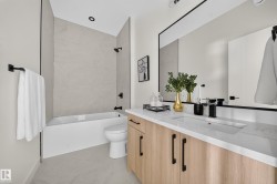 Contemporary bathroom featuring a light wood-finish vanity with black hardware, an integrated sink, and a white countertop - 