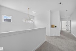 Upper-level hallway featuring a contemporary chandelier, recessed lighting, and light gray carpeting - 