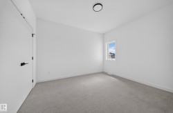 Neutral-toned carpeted room featuring a single window with white trim, a modern black ceiling light fixture, a white door with matte black hardware, and white baseboards - 