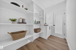 Expansive pantry featuring extensive white shelving, a built-in white cabinet with a countertop, a frosted glass door, and wood-finish flooring - 