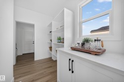 White built-in shelving, a single window, white lower cabinetry with black hardware, wood-finish flooring, and a white paneled door - 