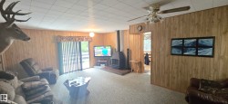 Interior featuring wood-paneled walls, a ceiling fan with integrated lighting, and a free-standing fireplace - 