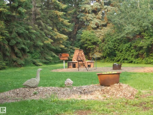 Expansive outdoor living area featuring a brick BBQ structure, a freestanding grill, a fire pit, and mature trees - 163062 Twp Rd 565, Rural Lamont County, AB 