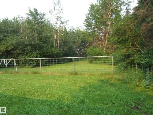 Expansive green lawn with a wire fence enclosing a grassy area, backed by mature trees and lush foliage - 163062 Twp Rd 565, Rural Lamont County, AB 