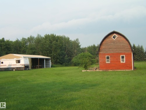 Red barn with gambrel roof, featuring wood siding on the upper portion and painted red siding on the lower portion, with two rectangular windows and a diamond-shaped upper window - 163062 Twp Rd 565, Rural Lamont County, AB 