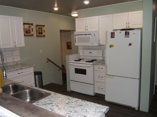 Kitchen featuring white cabinetry, white appliances, speckled countertops, stainless steel double-basin sink, and dark wood-finish flooring - 163062 Twp Rd 565, Rural Lamont County, AB 