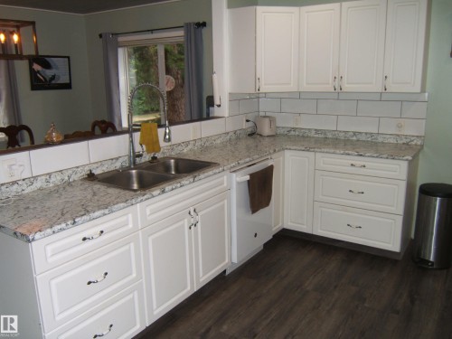 Modern kitchen featuring white shaker cabinetry, speckled countertops, a double basin stainless steel sink, and wood-finish flooring - 163062 Twp Rd 565, Rural Lamont County, AB 