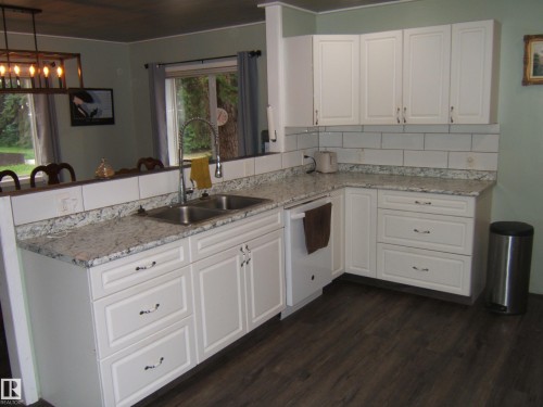 Kitchen featuring white shaker-style cabinetry, light-toned countertops, subway tile backsplash, a stainless steel double-basin sink with a gooseneck faucet, and dark wood-finish flooring - 163062 Twp Rd 565, Rural Lamont County, AB 