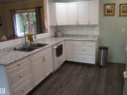 Kitchen featuring white cabinetry, speckled countertops, a subway tile backsplash, a double basin stainless steel sink with a high-arch faucet, and wood-finish flooring - 163062 Twp Rd 565, Rural Lamont County, AB 