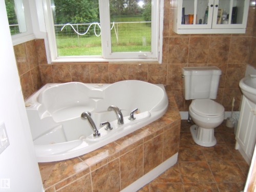 Corner soaking tub with deck-mounted chrome fixtures, surrounded by earth-toned square tile - 163062 Twp Rd 565, Rural Lamont County, AB 
