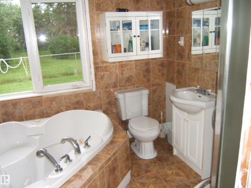 Bathroom featuring a jetted soaking tub, ceramic tile flooring, and a pedestal sink with a white cabinet vanity - 163062 Twp Rd 565, Rural Lamont County, AB 