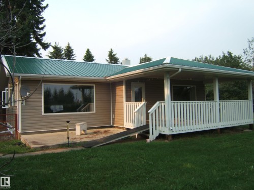Ranch-style residence featuring a green metal roof, light brown horizontal siding, and a covered front porch with white railing - 163062 Twp Rd 565, Rural Lamont County, AB 