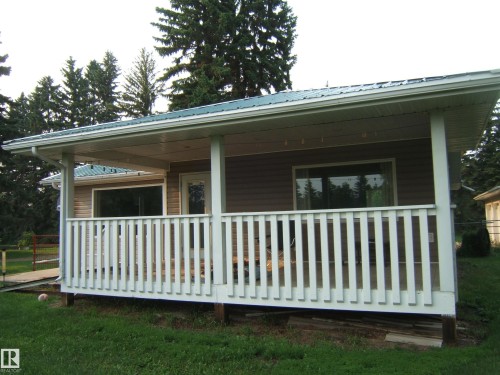 Covered front porch with white railings, brown siding, a green metal roof, and large windows - 163062 Twp Rd 565, Rural Lamont County, AB 