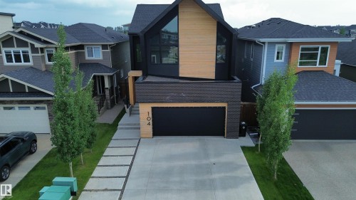 Modern residence featuring a striking black and wood-finish facade, an integrated garage with a black door, and a concrete driveway - 104 Edgewater Circle, Leduc, AB 