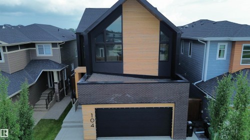 Modern exterior featuring black siding, natural wood-finish paneling, dark brick accents, a flat roof section, and an integrated garage door - 104 Edgewater Circle, Leduc, AB 