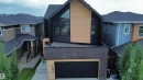 Modern exterior featuring black siding, natural wood-finish paneling, dark brick accents, a flat roof section, and an integrated garage door - 104 Edgewater Circle, Leduc, AB 