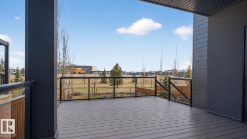 Spacious outdoor deck featuring composite flooring, dark-toned support pillars, and glass panel railings - 104 Edgewater Circle, Leduc, AB 
