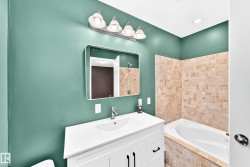 Bathroom featuring a white vanity with integrated sink, rectangular mirror, and an adjacent built-in bathtub with stone-look tile surround - 